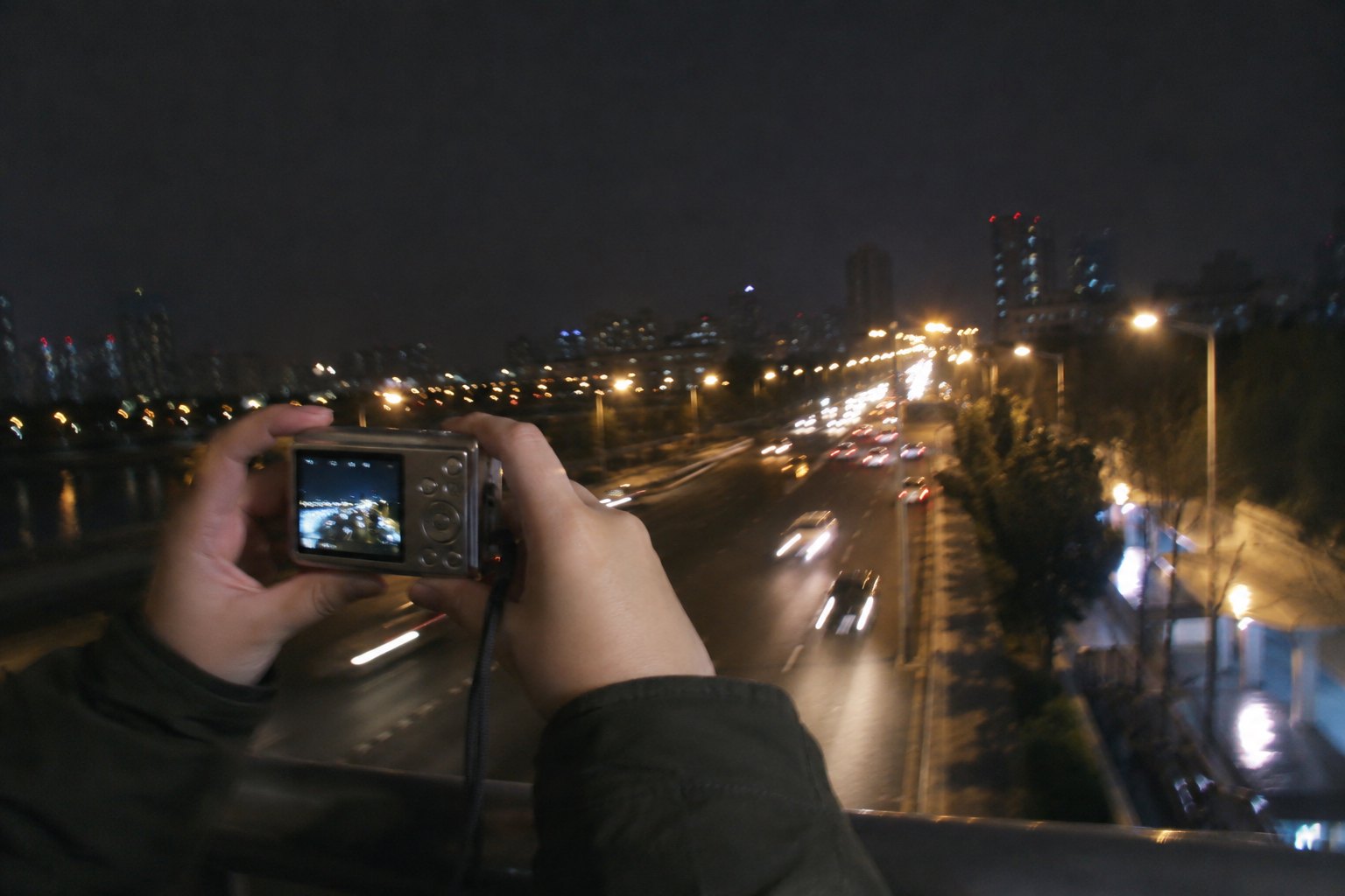 双手持便携数码相机拍摄夜间道路,路灯和车灯留下轻微光轨
