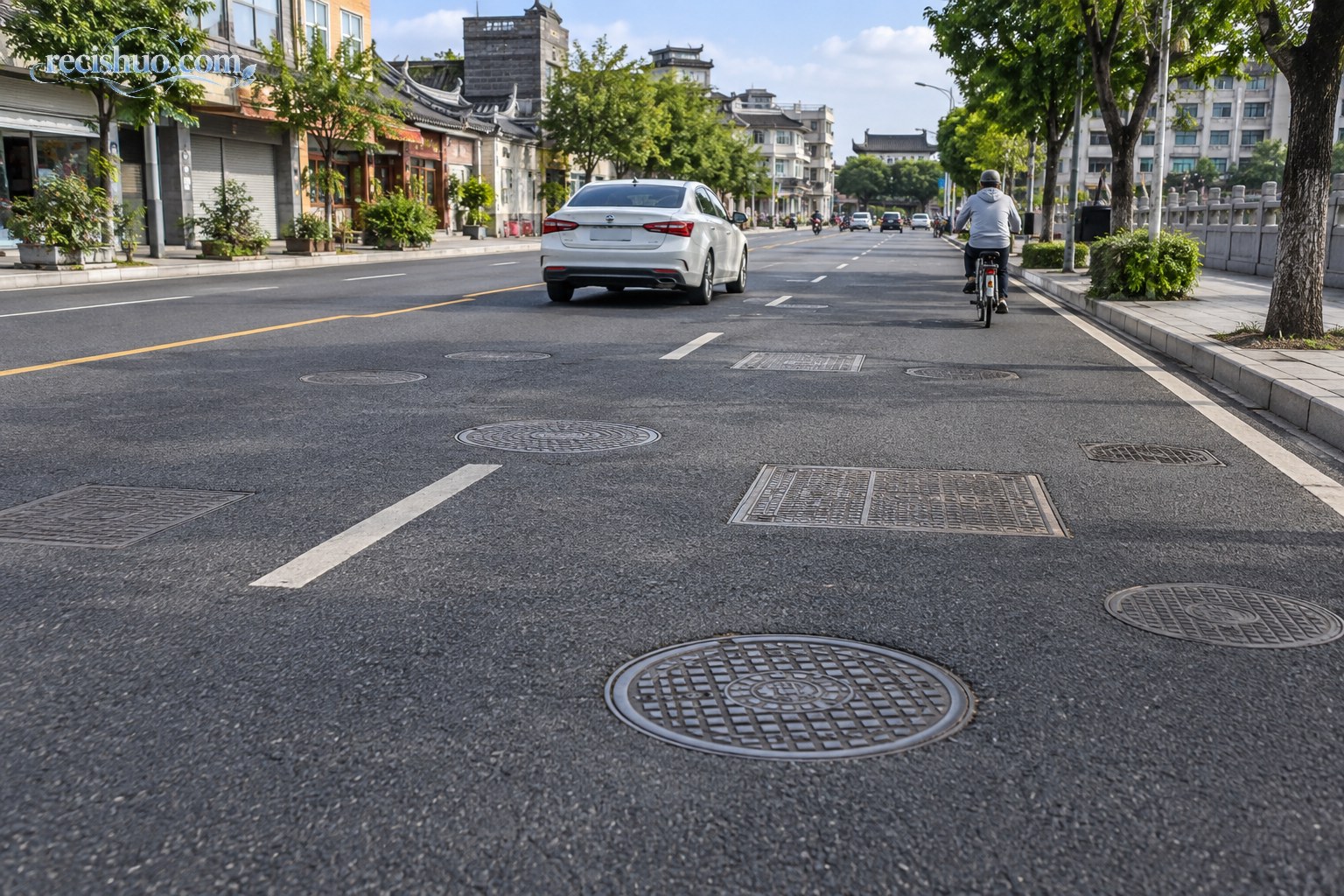 城市道路上分布着多个圆形和方形井盖,车辆与骑行者正常通行
