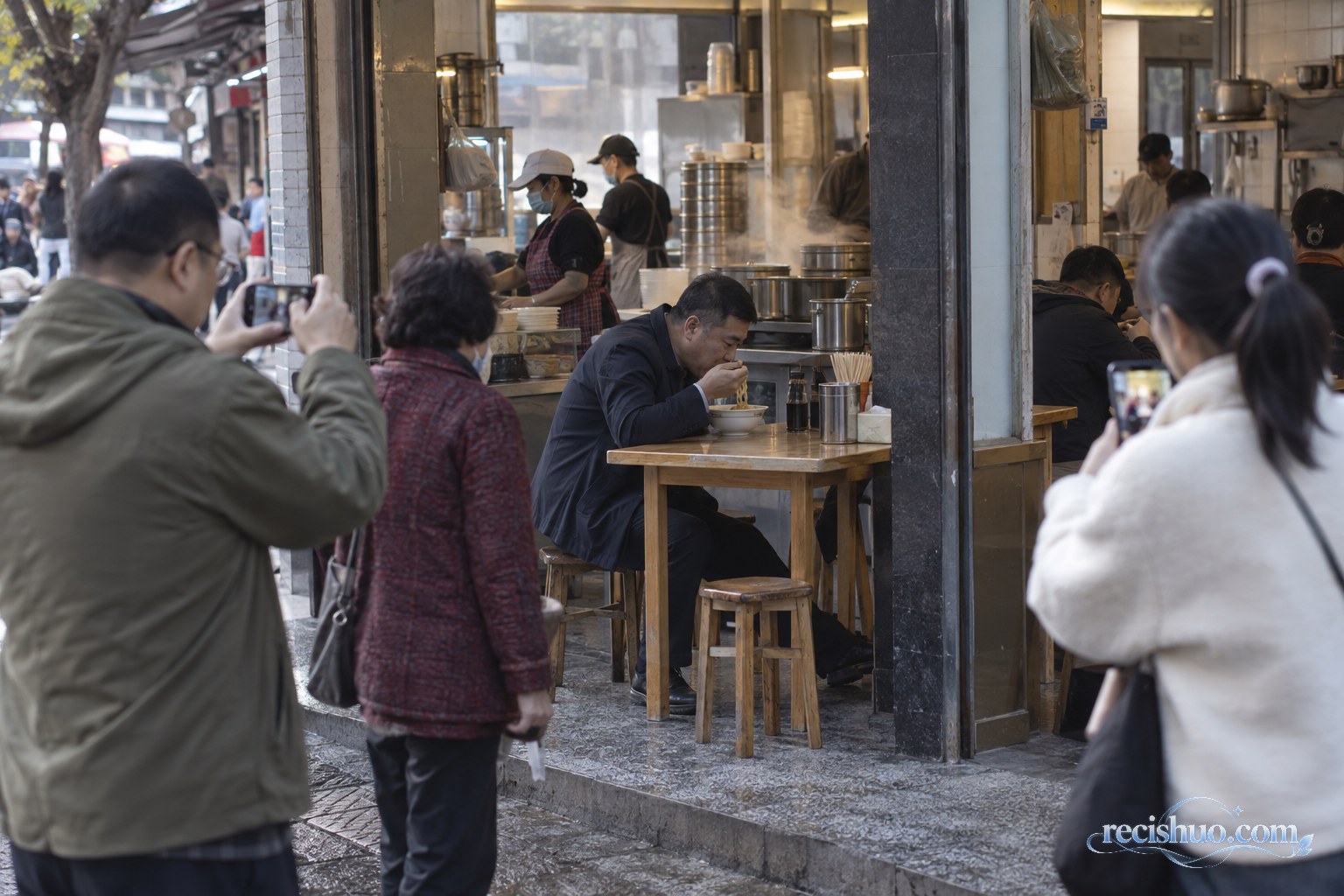 街坊早餐铺里一名男子正在吃面,几位路人在店外用手机记录