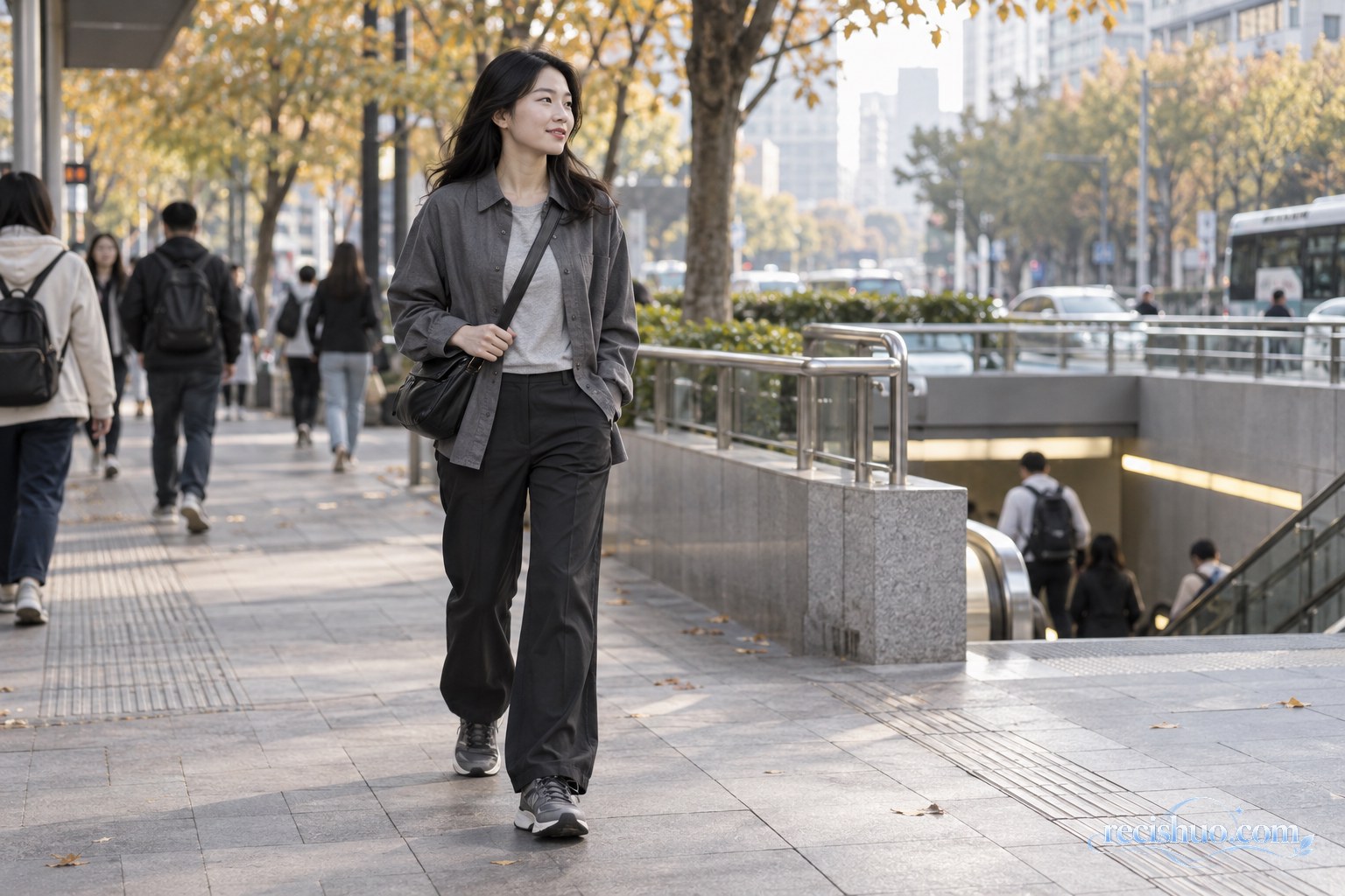 年轻女孩穿浅灰上衣、深灰外套和黑色长裤走在秋日城市街头