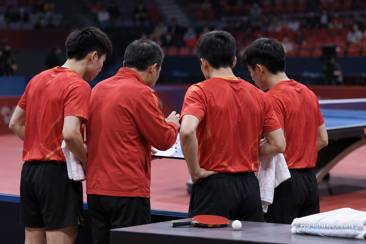 乒乓球男团赛前,三名队员与教练在球台旁商议阵容