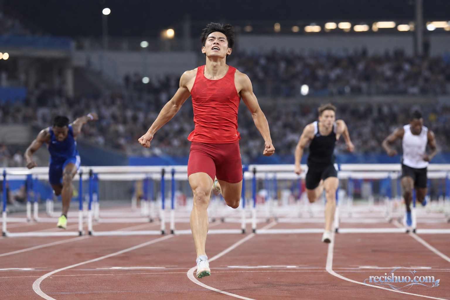 夜间体育场内一名身穿红色比赛服的男子跨栏运动员率先冲过终点