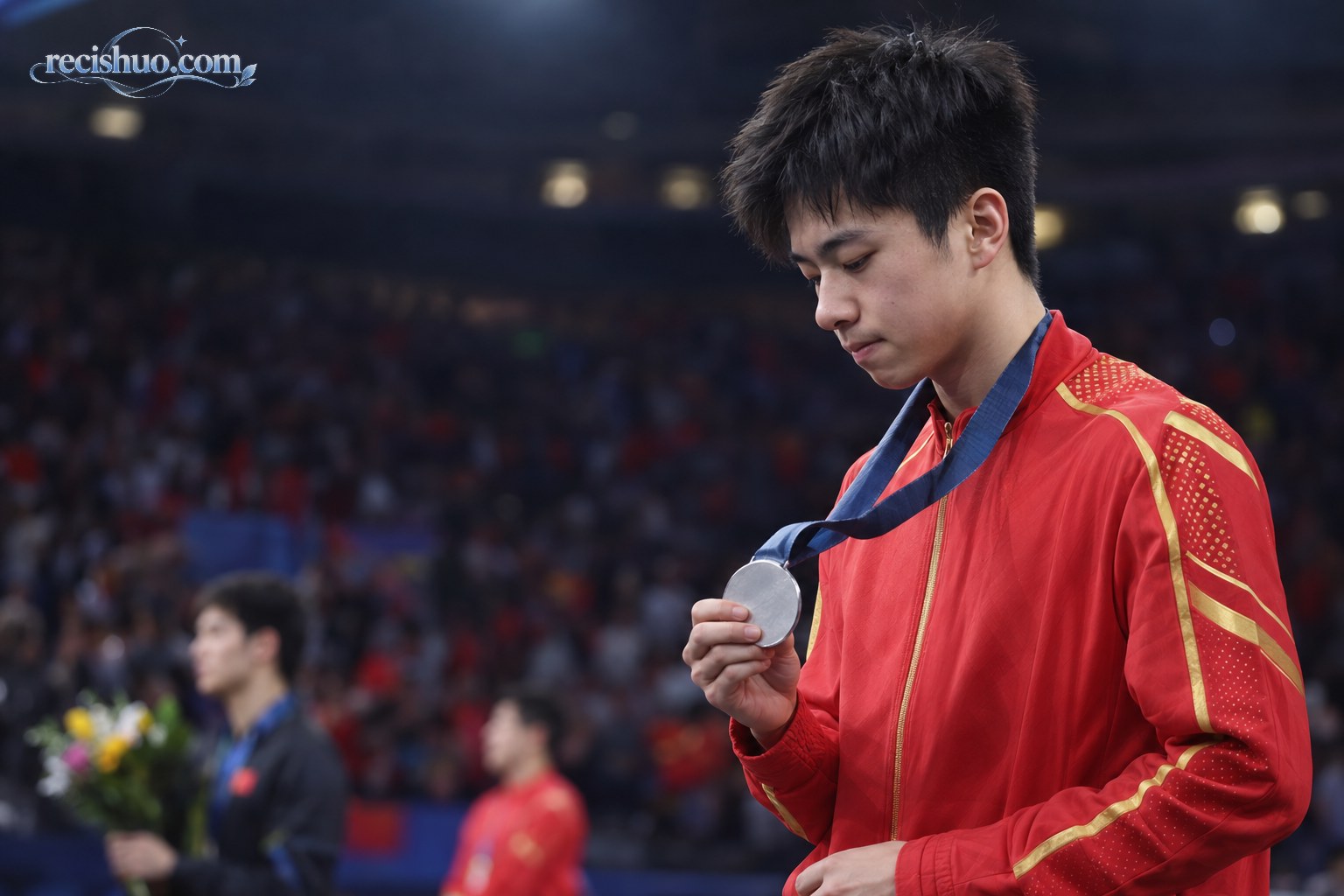 乒乓球赛后颁奖现场,一名年轻男子运动员低头握着刚摘下的银色奖牌