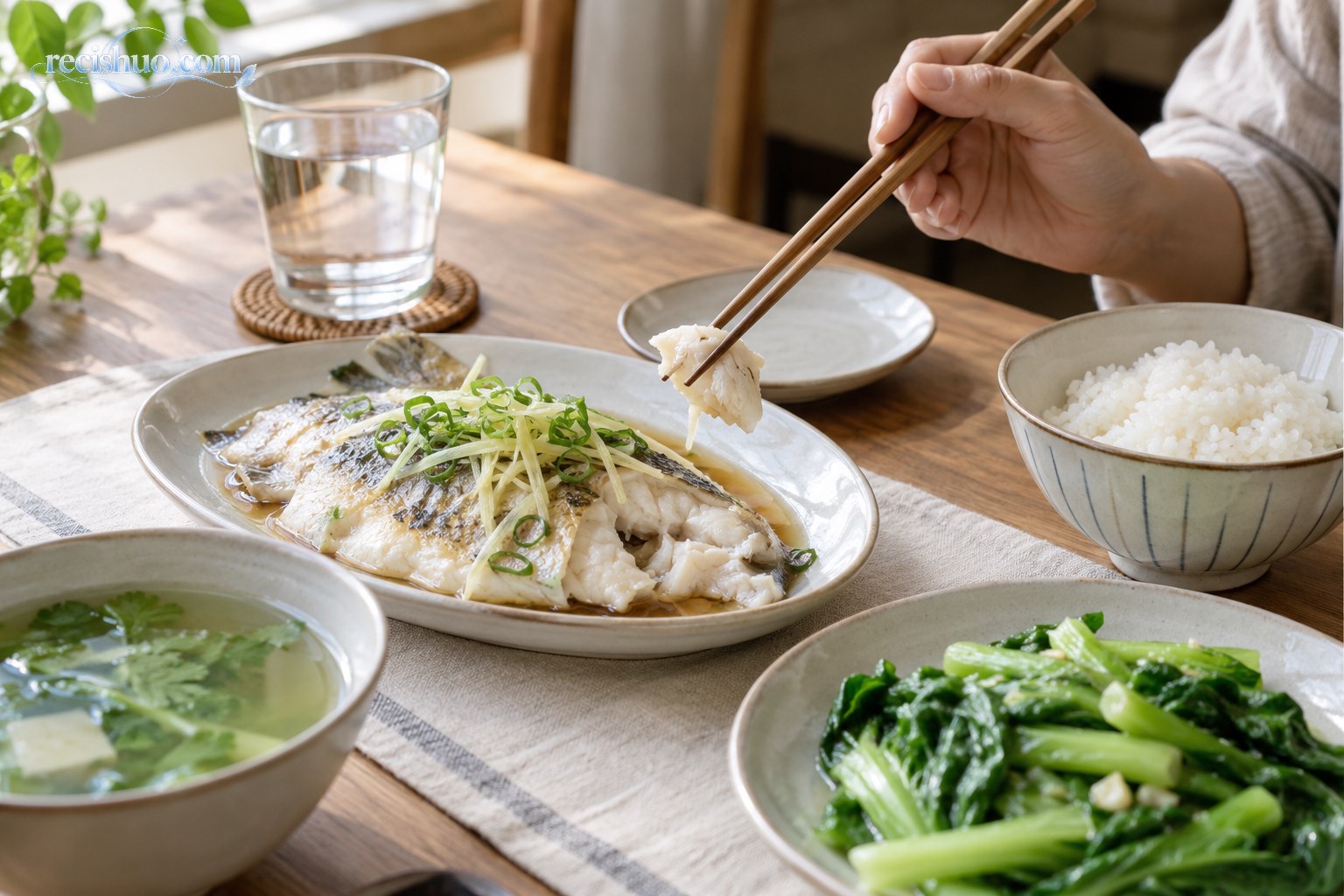 食客用筷子小口品尝清蒸鱼,桌上搭配米饭、青菜、清汤和温水