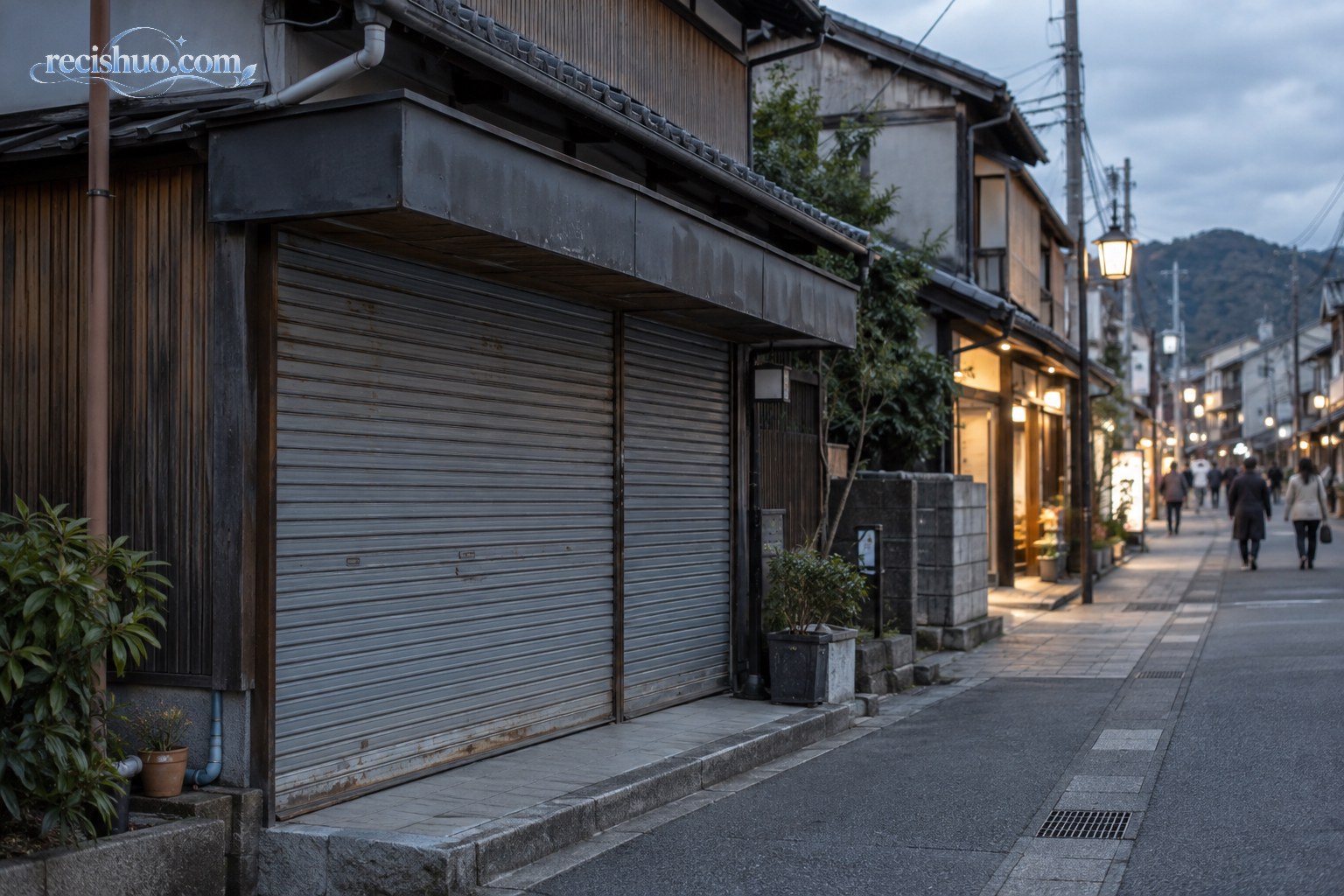 日本传统商业街上一家卷帘门紧闭的店铺,周边仍有少量行人与营业门店