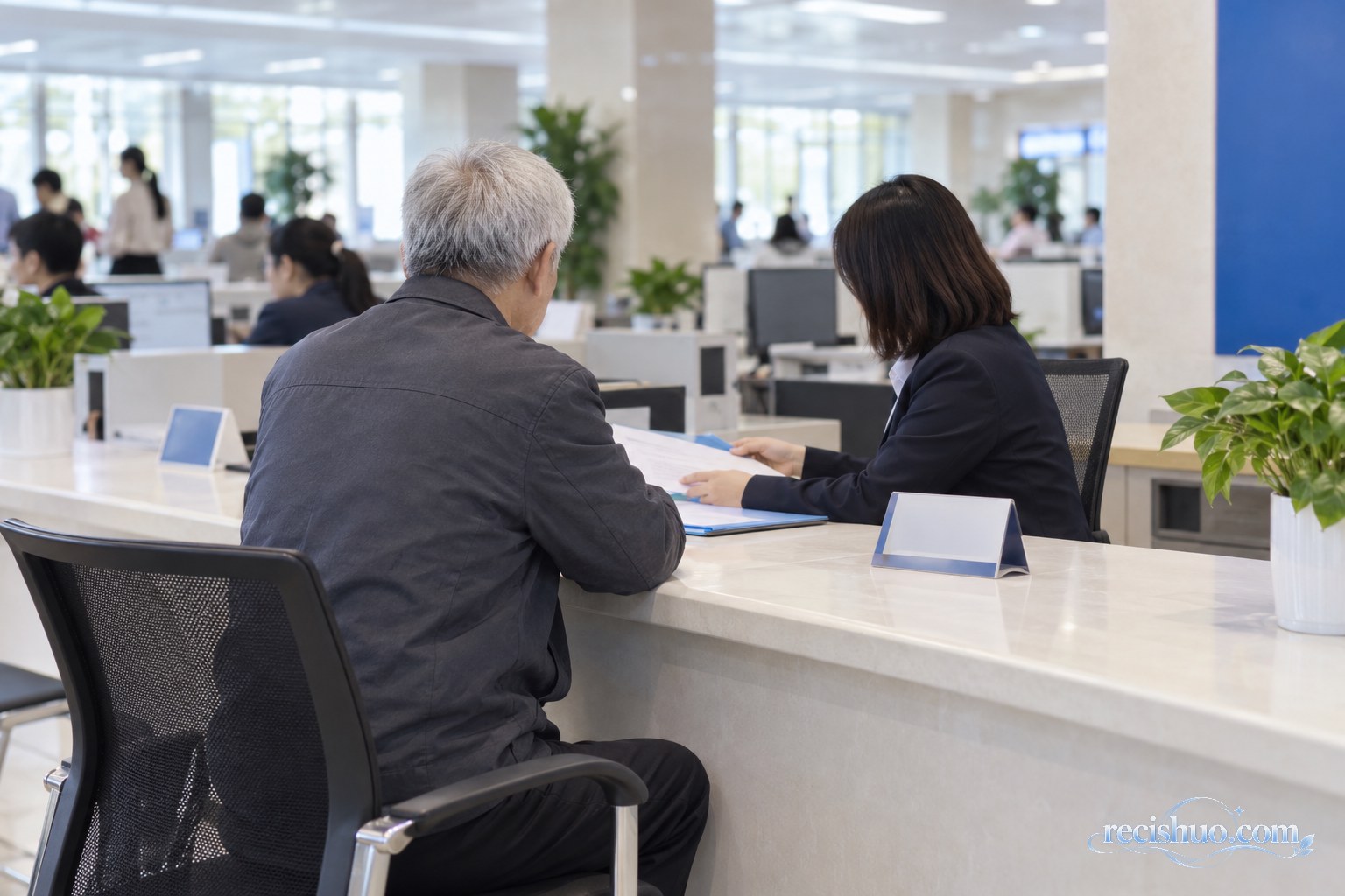 一位白发老人背对镜头在公共服务大厅向工作人员咨询手续