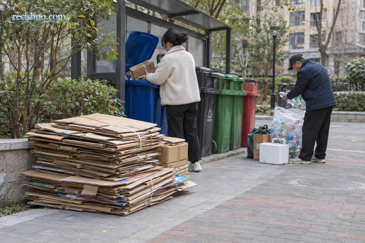 居民小区回收区域旁堆放着整理好的废旧纸箱,两名居民各自分类投放可回收物