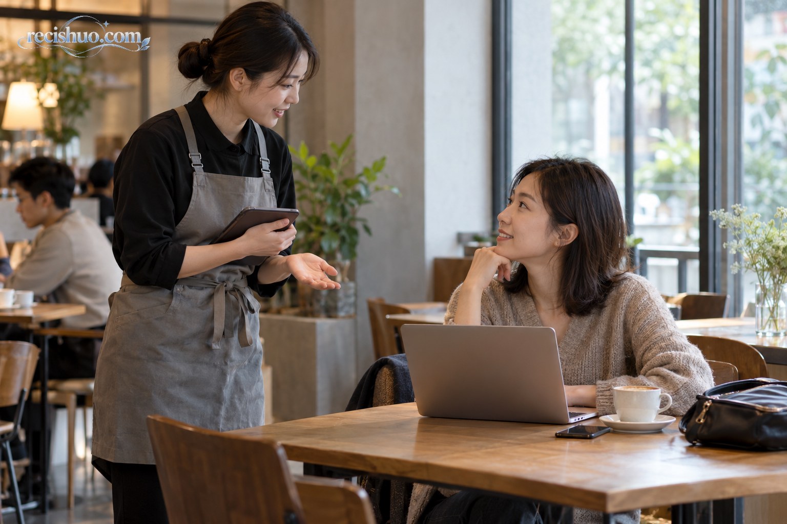 咖啡店员工在桌旁礼貌地与使用电脑的顾客沟通